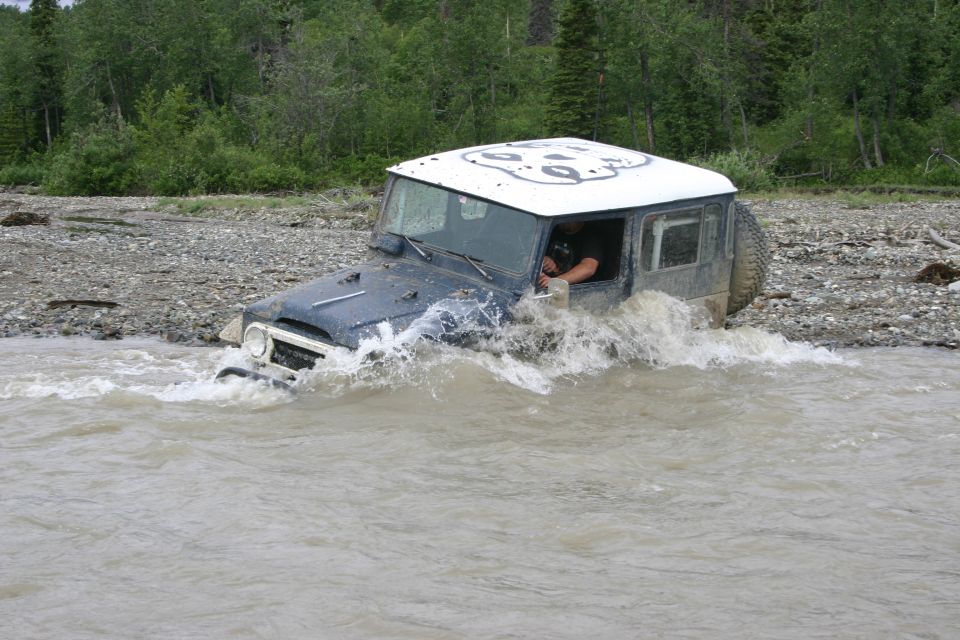 Dark blue SUV with white roof driving through murky water, front grille visible
