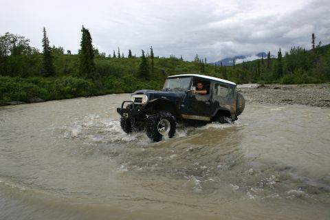 2003 Jeep TJ - Driver navigates a Jeep Wrangler TJ through a rocky riverbed under a cloudy sky.