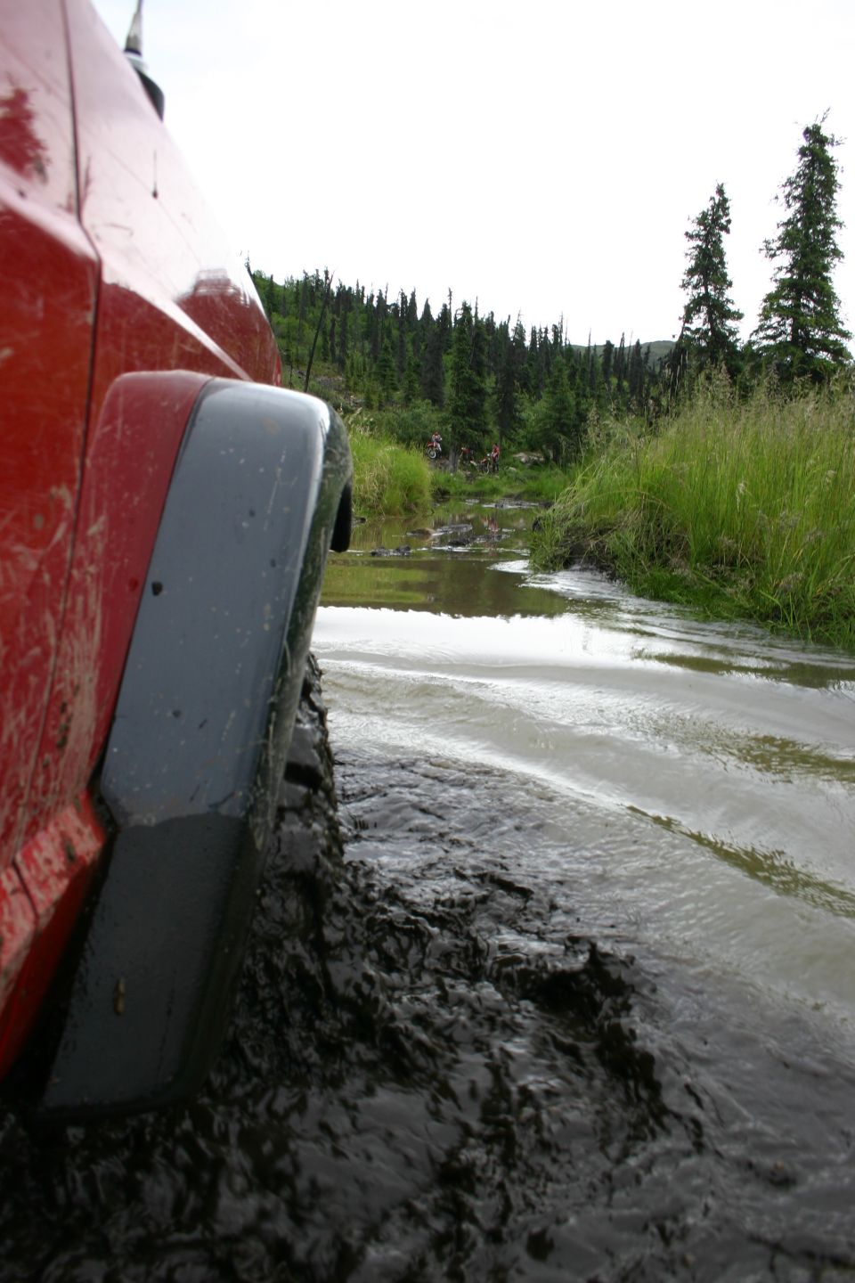 Red 2003 Jeep TJ driving through mud and water on a trail