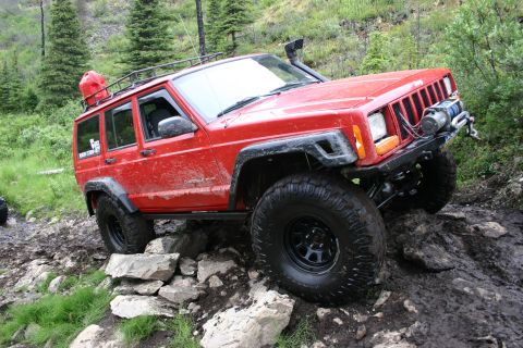2003 Jeep TJ - Red Jeep Cherokee XJ navigates a challenging rocky trail with a winch and roof rack.