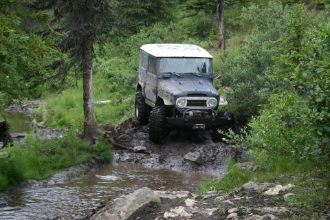 2003 Jeep TJ - This classic Toyota Land Cruiser navigates a challenging muddy path in a forest setting.