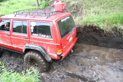 2003 Jeep TJ - A red Jeep Wrangler TJ navigates a muddy trail, demonstrating its off-road capabilities.