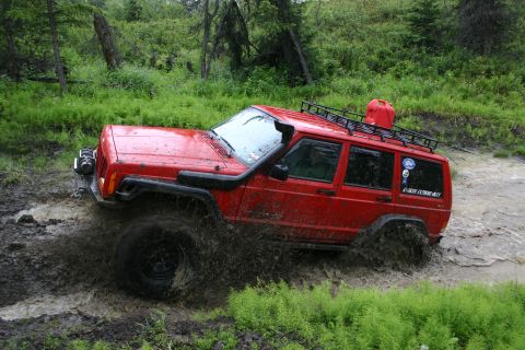 2003 Jeep TJ - A red Jeep Cherokee XJ navigates a muddy trail with a snorkel and roof rack.