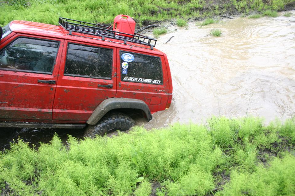 Red Jeep Cherokee XJ side view driving through muddy water with a red jerry can on the roof rack