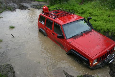 2003 Jeep TJ - Red Jeep Cherokee with roof rack and snorkel is stuck in a muddy water hole.