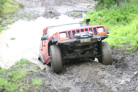 2003 Jeep TJ - A red 2003 Jeep TJ is stuck in a muddy off-road trail, its front end partially submerged in water and mud.