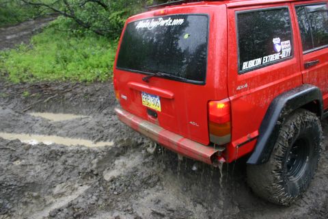 2003 Jeep TJ - Red Jeep Cherokee XJ stuck in mud on a trail, showing "Rubicon Extreme-Duty" sticker.