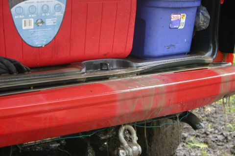 2003 Jeep TJ - Mud-splattered rear bumper and cargo area of a vehicle with red and blue storage bins.