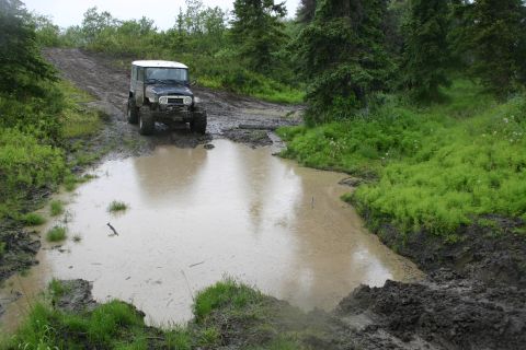 2003 Jeep TJ - Off-road vehicle navigates a muddy track with a large puddle.