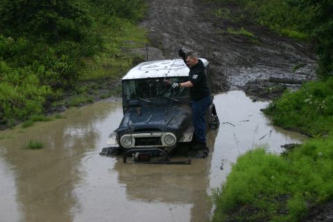 2003 Jeep TJ - A man attempts to free a mud-covered Toyota Land Cruiser FJ40 from a water-filled rut.