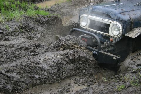 2003 Jeep TJ - An off-road vehicle navigates a challenging muddy terrain, with water and mud spraying around its front.