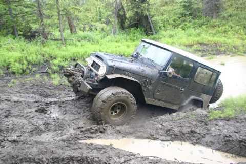 2003 Jeep TJ - This off-road vehicle is deeply embedded in mud, with its front end partially submerged and its tires struggling for traction.