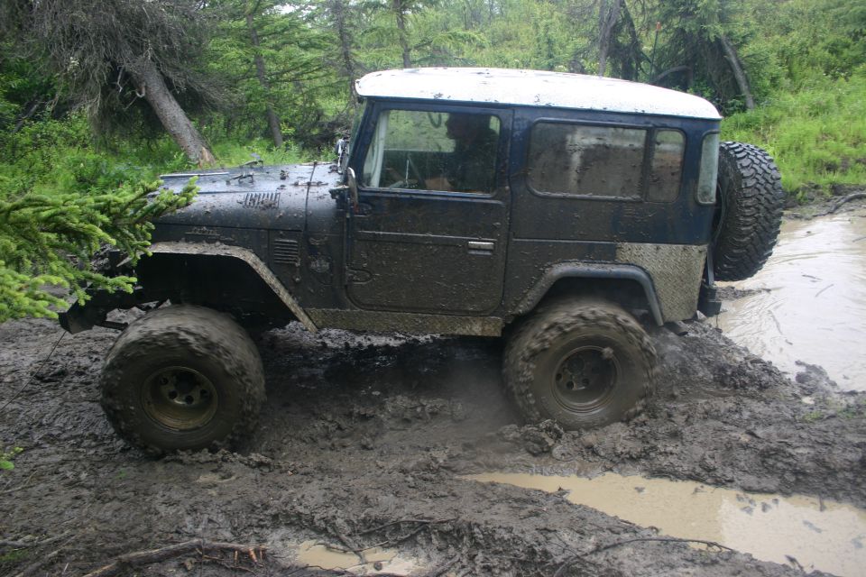 Mud-covered off-road vehicle stuck in mud with trees in background