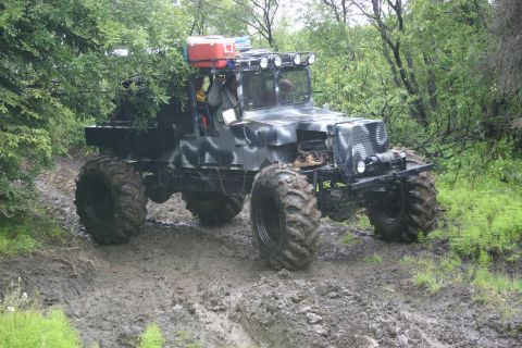 2003 Jeep TJ - Custom off-road vehicle with large tires navigating a muddy trail in a wooded area.