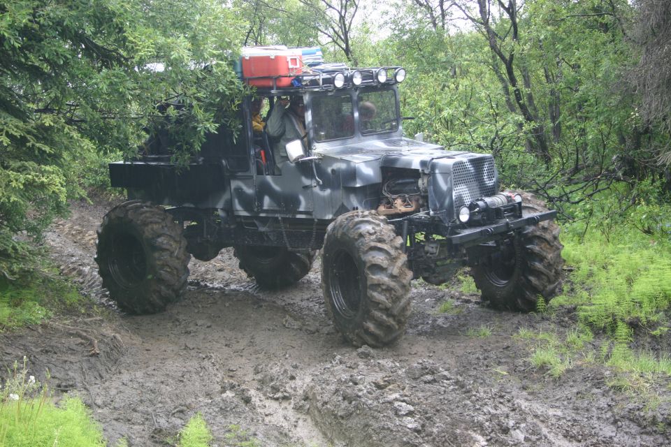 Custom off-road vehicle with large tires driving on a muddy trail through trees
