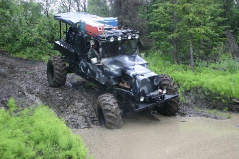 2003 Jeep TJ - A heavily modified off-road vehicle navigates a muddy trail with deep water obstacles.