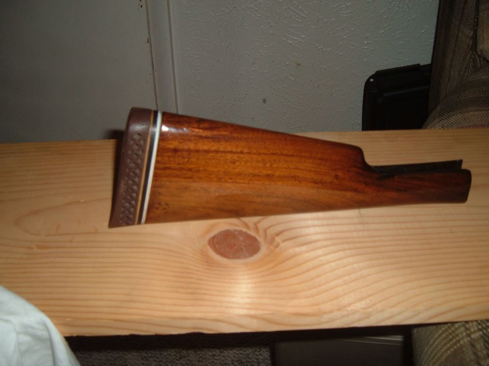Refinished walnut shotgun buttstock with checkered butt plate resting on a pine board