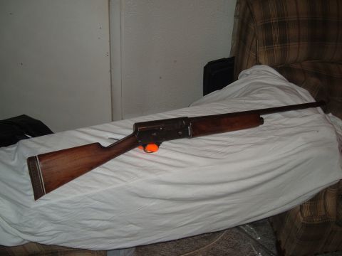 1919 Yugo Vega - A shotgun with a wooden stock and forend is displayed on a white sheet. The trigger guard is bright orange.