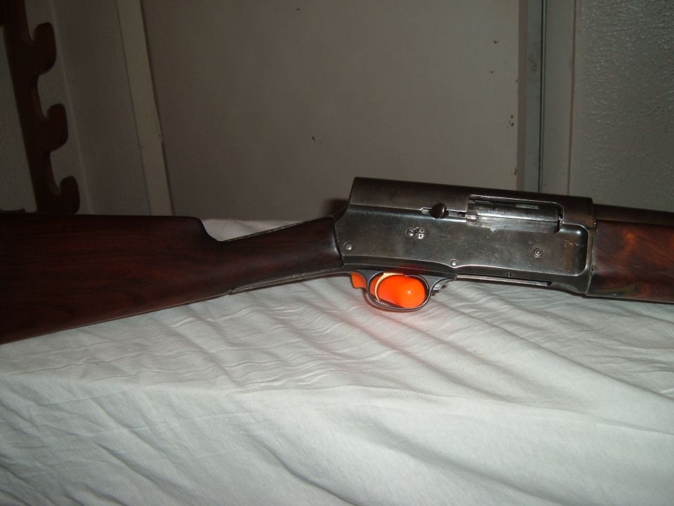 Vintage semi-auto shotgun with wood stock and orange trigger cover on white cloth