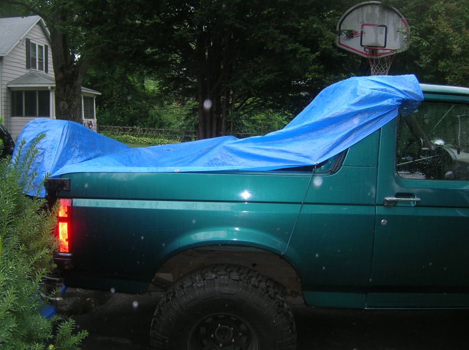 Green SUV with a blue tarp covering its roof and rear, side view