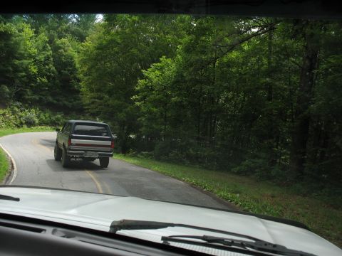 1995 Ford C-350 (Centurion Conversions) - A Ford Bronco drives on a curved road surrounded by lush green trees.