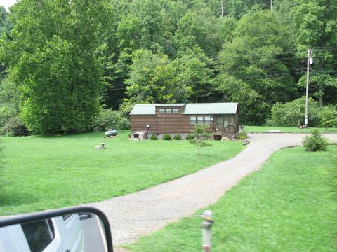 1995 Ford C-350 (Centurion Conversions) - A view of a cabin in a wooded area, with a gravel driveway in the foreground.