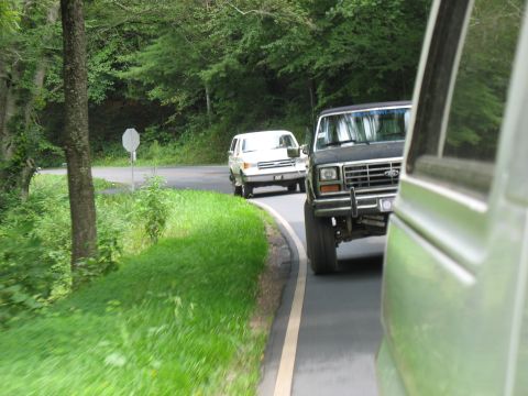 1995 Ford C-350 (Centurion Conversions) - Two vehicles travel down a winding road surrounded by trees.