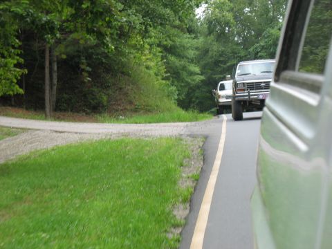 1995 Ford C-350 (Centurion Conversions) - A dark 1980s Ford F-Series truck is seen from the side, following another vehicle on a paved road.