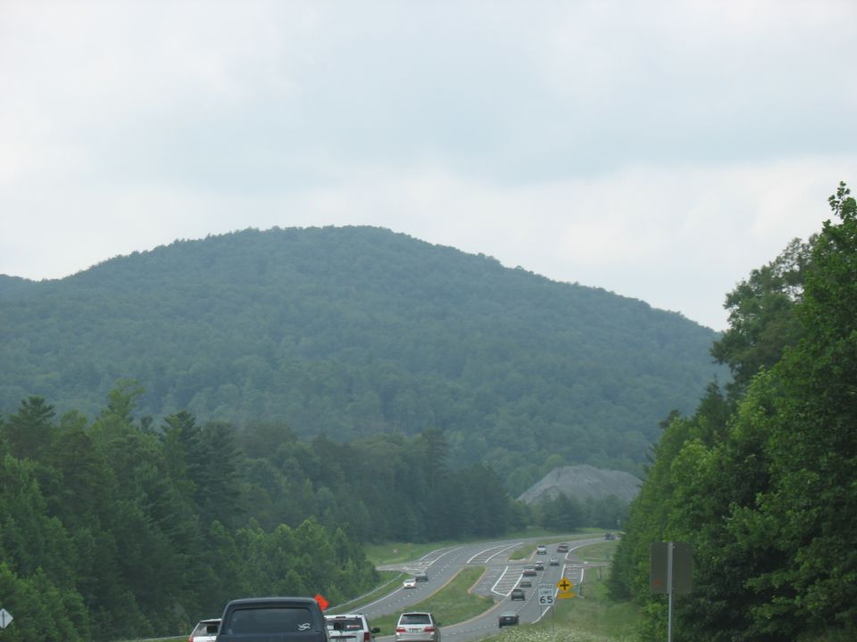 Highway with multiple vehicles driving past a forested mountain under a cloudy sky
