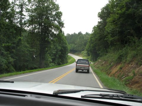 1995 Ford C-350 (Centurion Conversions) - A pickup truck drives on a winding road surrounded by trees.