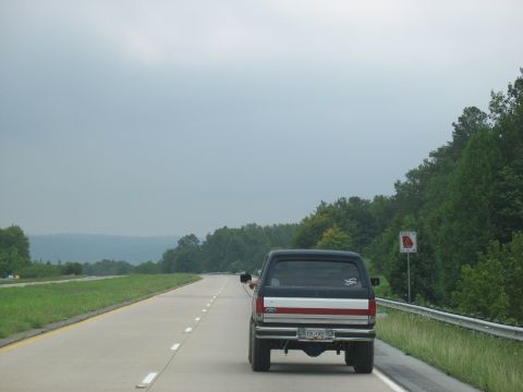 1995 Ford C-350 (Centurion Conversions) - Rear view of a black pickup truck with a red and white stripe on the tailgate, driving on a highway.