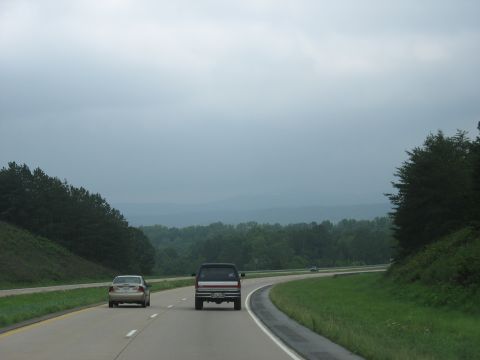 1995 Ford C-350 (Centurion Conversions) - Vehicles travel down a highway surrounded by trees and distant hills on an overcast day.