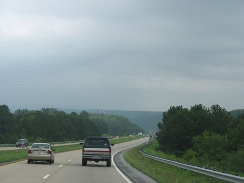 1995 Ford C-350 (Centurion Conversions) - A pickup truck travels down a highway under an overcast sky, with a speed limit sign indicating 65 mph.