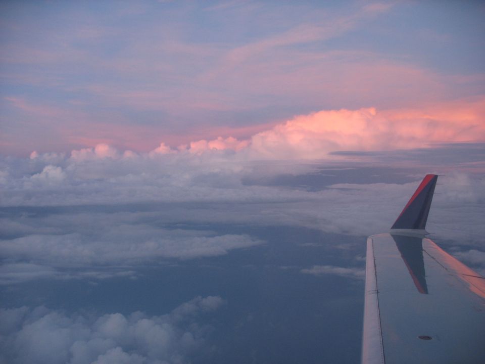 Airplane wing visible against a sky with pink and purple clouds at sunset