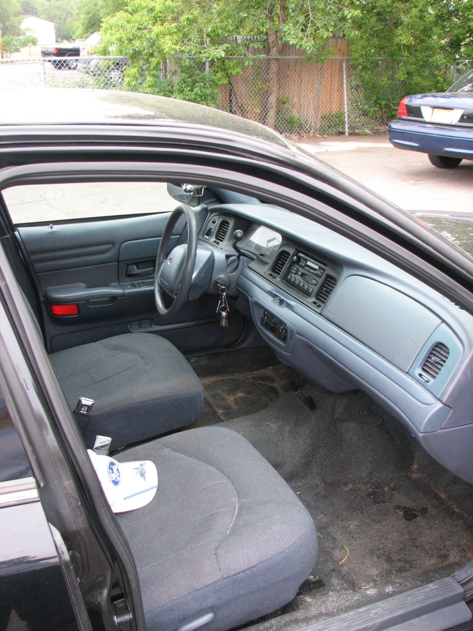 Interior shot of a 2000 Ford Crown Victoria, showing the dashboard, steering wheel, and front seats. Another car is visible in the background