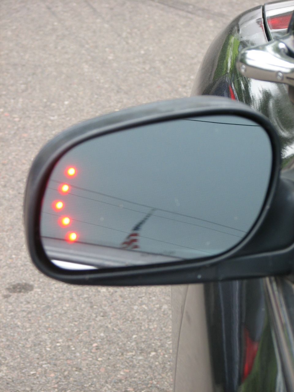 Driver's side mirror on black car with row of red LED turn signal lights lit in the glass