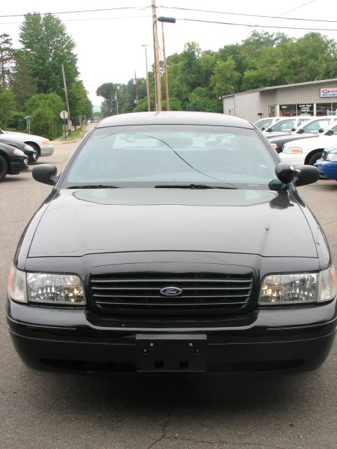 2000 Ford Crown Victoria - A black 2000 Ford Crown Victoria is shown from the front, parked in front of a building with other vehicles visible.