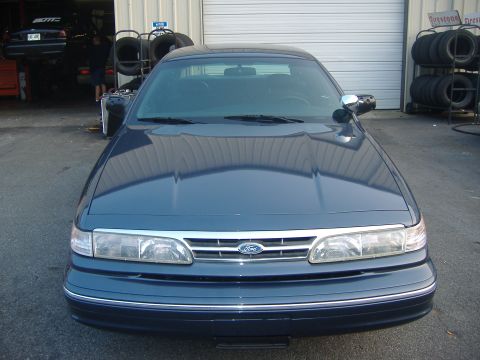 2001 Ford Crown Victoria - A dark blue 2001 Ford Crown Victoria is parked in front of a garage, with another vehicle visible on a lift inside.