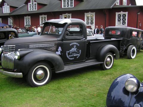 1978 Ford Bronco - A classic black pickup truck, adorned with custom artwork, is seen towing a vintage sedan at an outdoor event.