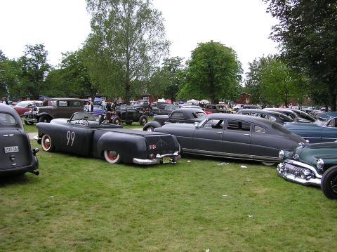 1978 Ford Bronco - A unique black custom car with a trailer bed, marked with the number 99, is parked on a grassy field among other vehicles.