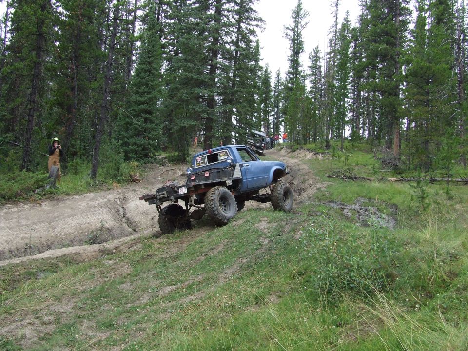 Blue pickup truck with large tires climbing a dirt hill, other vehicles in background