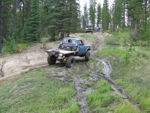 1990 Ford Bronco - Two trucks navigate a muddy trail through a forest.