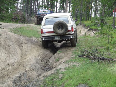 1990 Ford Bronco - A white 1990 Ford Bronco navigates a rutted dirt path during an off-road event, with another vehicle following.
