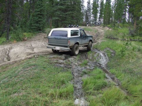 1990 Ford Bronco - Ford Bronco navigates a challenging muddy path through a wooded area.