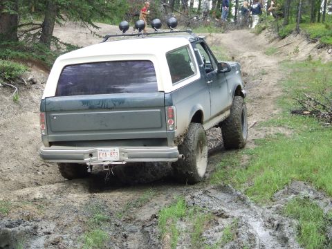 1990 Ford Bronco - Ford Bronco navigates a challenging muddy off-road course with onlookers in the background.