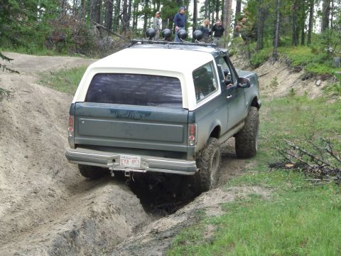 1990 Ford Bronco - This SUV navigates a challenging off-road trail with a white removable top and roof-mounted lights.