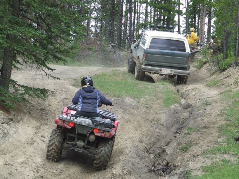 1990 Ford Bronco - An ATV and a Ford Bronco navigate a rutted dirt path through a wooded area.