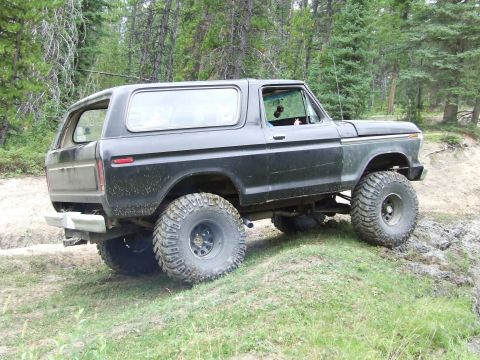 1990 Ford Bronco - This lifted Ford Bronco is navigating a muddy, off-road trail surrounded by dense forest.