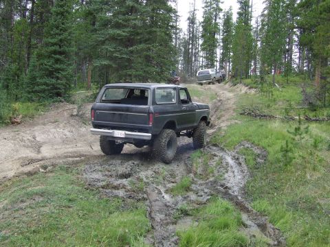 1990 Ford Bronco - A dark-colored Ford Bronco navigates a muddy off-road trail with other vehicles in the background.