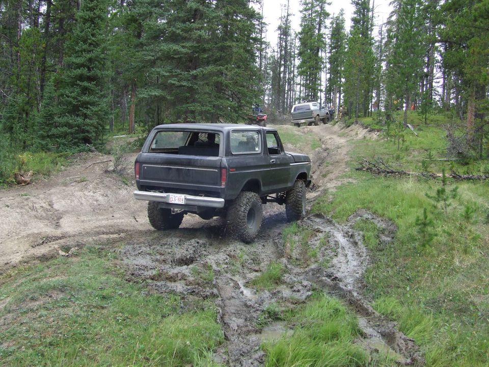 Black Ford Bronco with large tires driving on a muddy trail, rear view